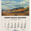 Load image into Gallery viewer, Vintage Union Pacific Railroad calendar page for November 1969, featuring a painted landscape of a yellow freight train traveling through mountains under a cloudy sky, with a monthly calendar grid and centennial text below.
